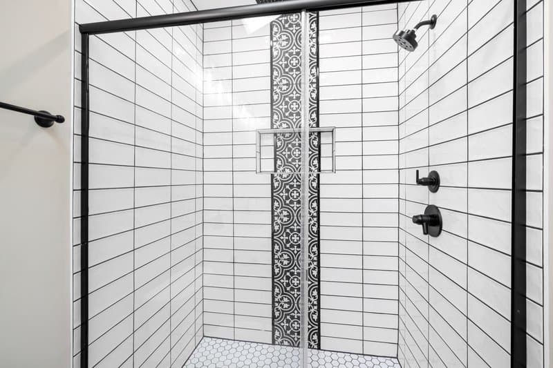 A white subway-tile shower with a patterned accent strip and black fixtures