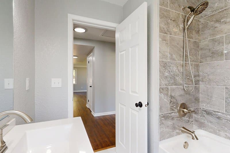 A tub-shower with gray tile and brushed nickel fixtures in a remodeled hall bath