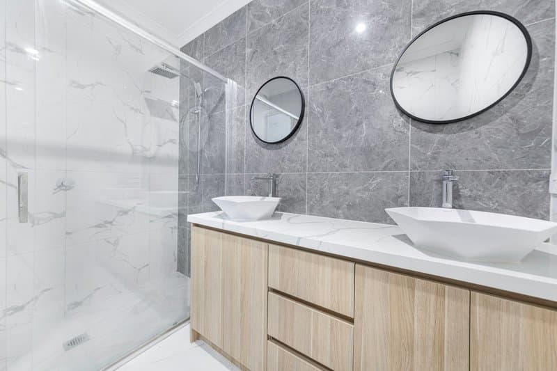 A double vanity with vessel sinks and round mirrors on gray marble tile