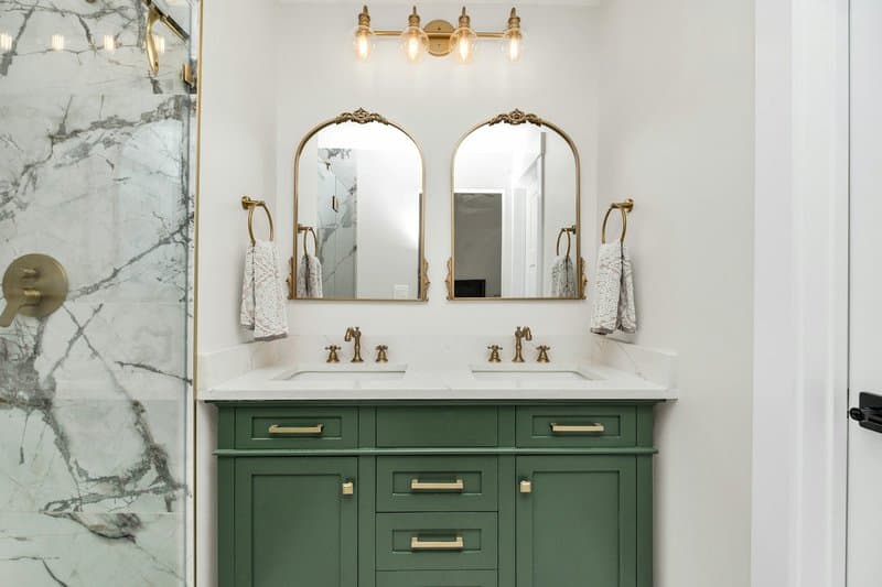 A green vanity with brass hardware, double sinks, and arched mirrors