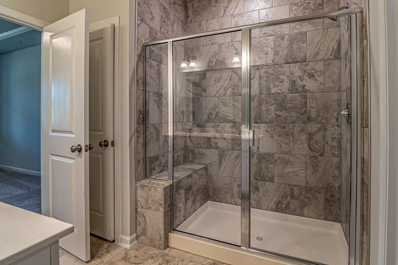 A walk-in shower with gray stone tile, a built-in bench, and a framed glass door