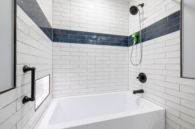 A tub-shower with white subway tile, a navy accent band, and matte black fixtures