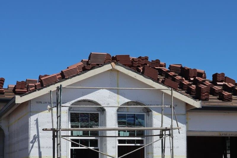 Bundles of clay roof tiles staged along the ridge of a house under construction