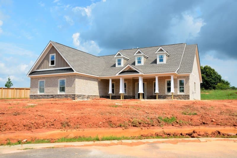 A newly built brick home with a gray asphalt shingle roof and three dormers