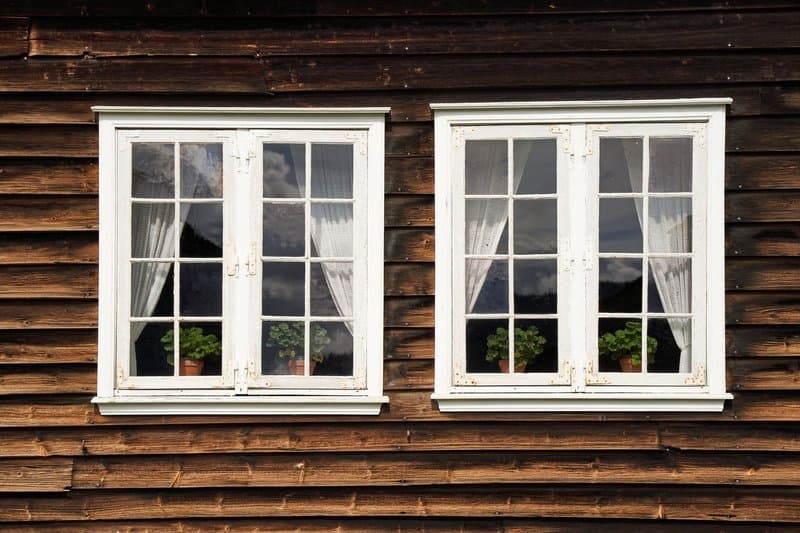 Two white-framed multi-pane windows on a dark wood cabin wall