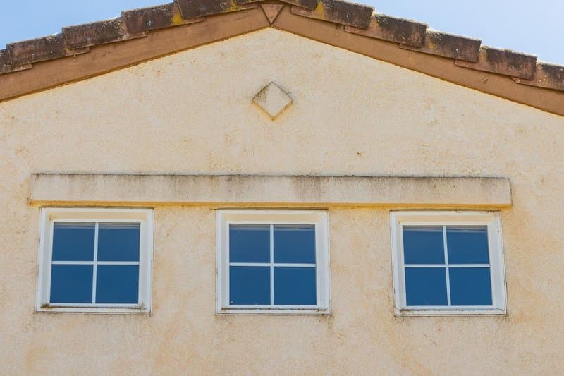 Three grid-pane windows on a sunlit stucco gable