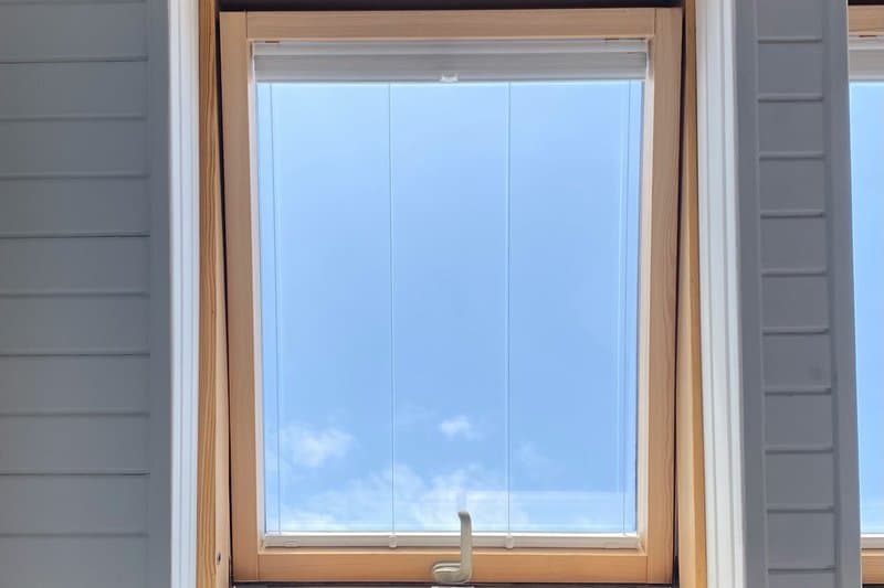 A wood-framed awning window on white lap siding, open to a blue sky