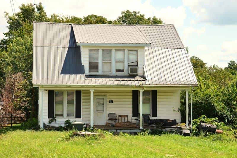 A white farmhouse with a standing-seam metal roof, a dormer, and a front porch